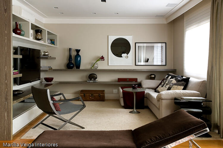 home theater integrado com prateleira em madeira escura, vários objetos de decoração como vasos e quadro, sofá claro e poltrona geometrica