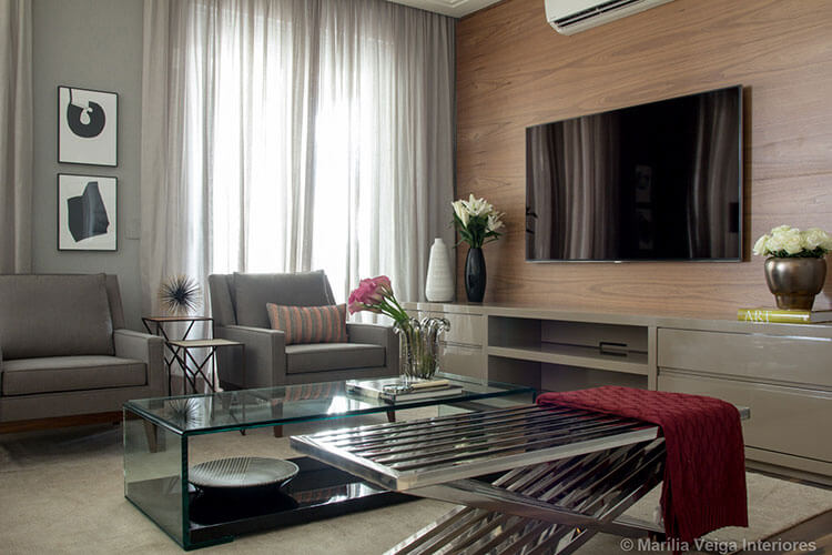 home theater integrado, tv sob painel de madeira, poltronas cinzas, mesa de centro retangular de vidro