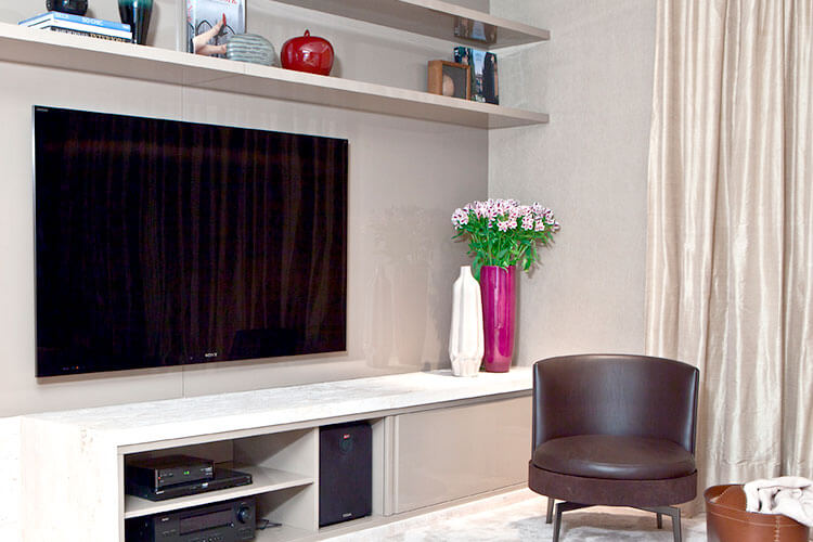home theater integrado tv em painel cinza claro com prateleiras em cima e poltrona ao lado redonda marrom