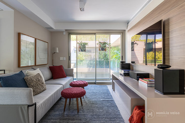 home theater integrado com painel da madeira atrás da tv, sofá cinza claro e elementos de decoração como almofadas e puffs em azul marinho e vinho