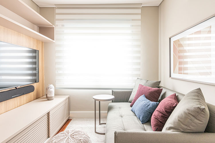 home theater integrado ambiente pequeno, bem iluminado, com painel de madeira atrás da tv, rack e sofá claros e almofadas azul e vinho