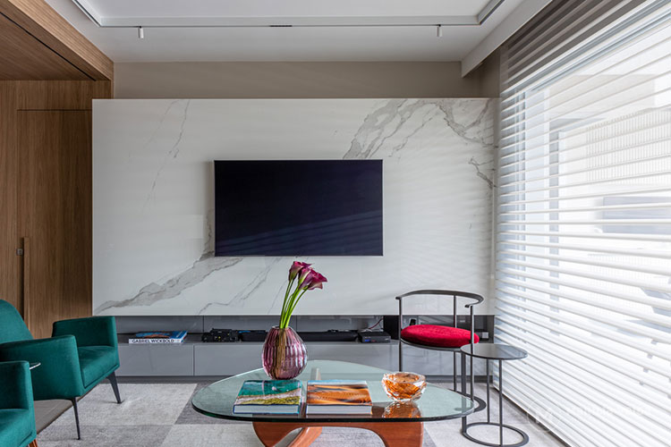 home theater integrado, tv sobre painel de pedra, poltronas em tom verde escuro e mesa de centro em formato irregular com pé de madeira e tampo de vidro