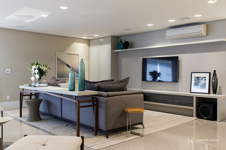 home theater integrado ao estar, com sofá cinza e aparador atrás com peças de decoração e flores