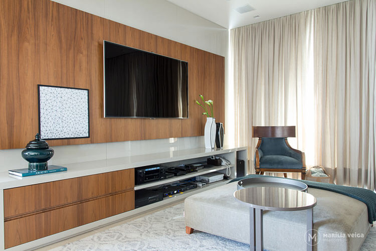 home theater com painel de madeira atrás da tv e cortina, móveis e tapete claros