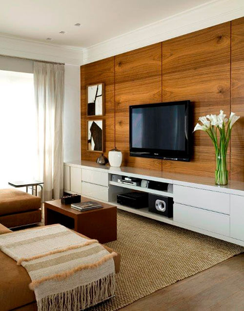home theater integrado tv e quadros em painel de madeira, rack branco com vasos como decoração e sofá e mesa de centro marrons