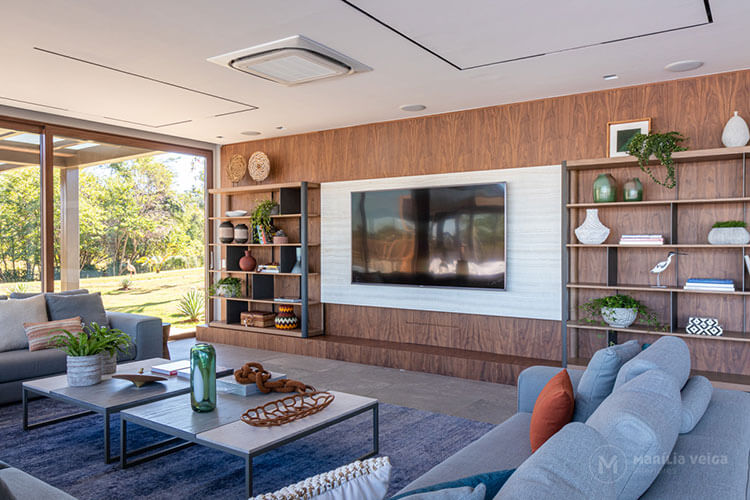 home theater integrado com televisão sobre smartstones, atrás um painel em marcenaria e sofá em ‘U’
