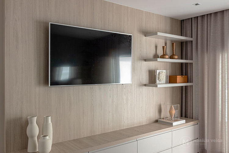 Detalhe da tv com painel de madeira clara, prateleiras ao lado e rack com gavetas