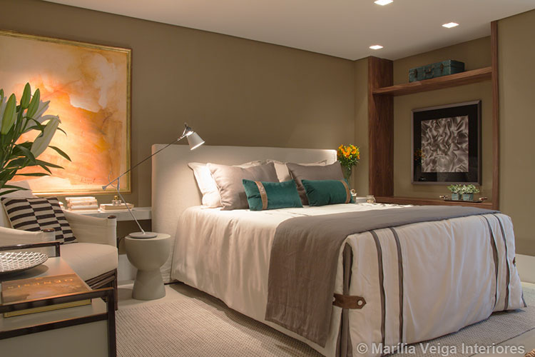 suítes de casal em tons nude mais escuros com quadros de decoração, poltrona e luminária ao lado da cama
