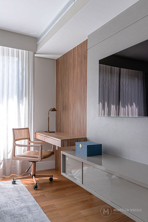 Detalhe canto trabalho ou estudo com mesa e painel em madeira, tv ao lado com painel e rack em tom cinza