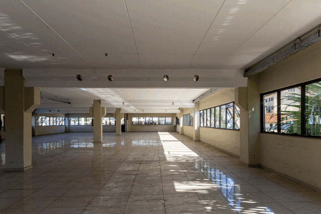 Foto de uma das lajes antes da reforma, ainda vazia e com piso cerâmico, mostrando o ritmo estrutural de pilares e a iluminação natural pelas janelas perimetrais. Este ponto de partida orientou o projeto de escritório corporativo: mapear fluxos, definir zonas de foco e convivência e planejar soluções que traduzissem a identidade do Efí Bank. A leitura clara do vão, da circulação e das entradas de luz permitiu criar, depois, ambientes integrados e convidativos — a base para a transformação que o time sentiria no dia a dia.