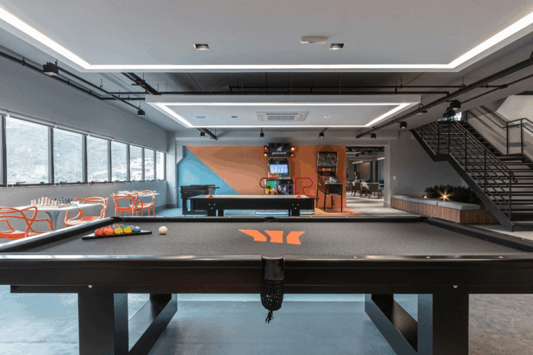 Área de descompressão do Efí Bank com mesa de bilhar, arcades e fundo laranja e azul