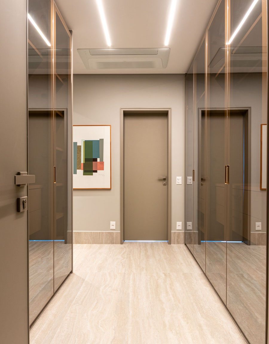 Closet sofisticado demais: portas em vidro refletente que abrem e fecham, interior generoso e organizado, acabamento que não grita mas fala. Quarto casal, Apartamento Jardim Paulista.