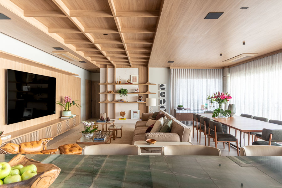 O coração do apartamento: cozinha integrada, bancada em verde , sala de estar com sofá generoso, sala de jantar ampla, teto ripado em madeira que unifica tudo. Projeto residencial Jardim Paulista.